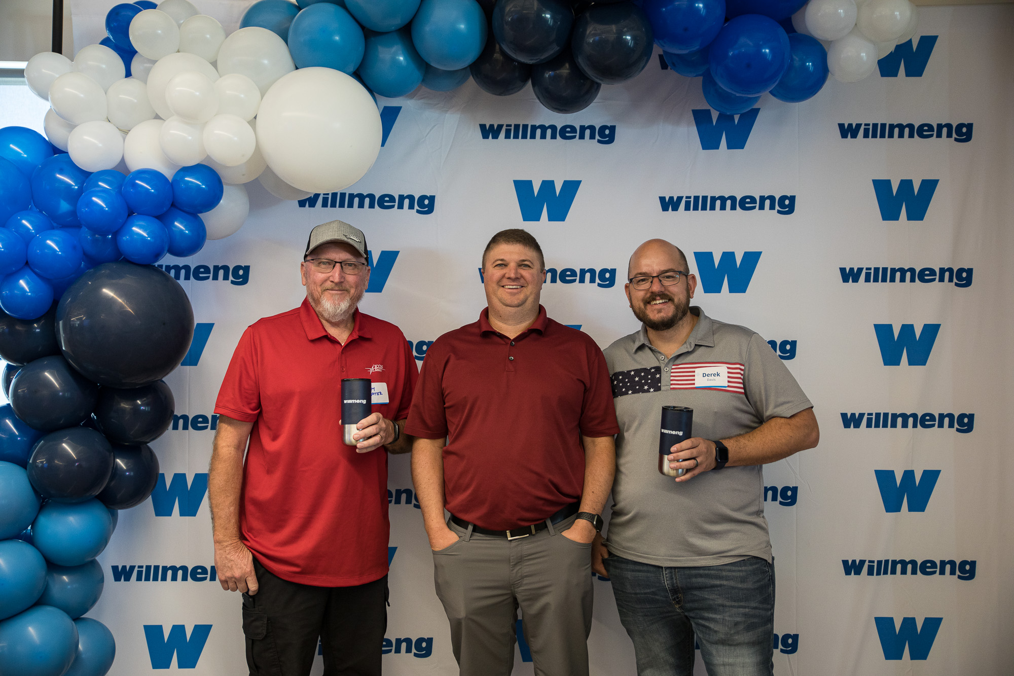 Three men standing in front of a Willmeng Trade Partner Appreciation Event banner with balloons.