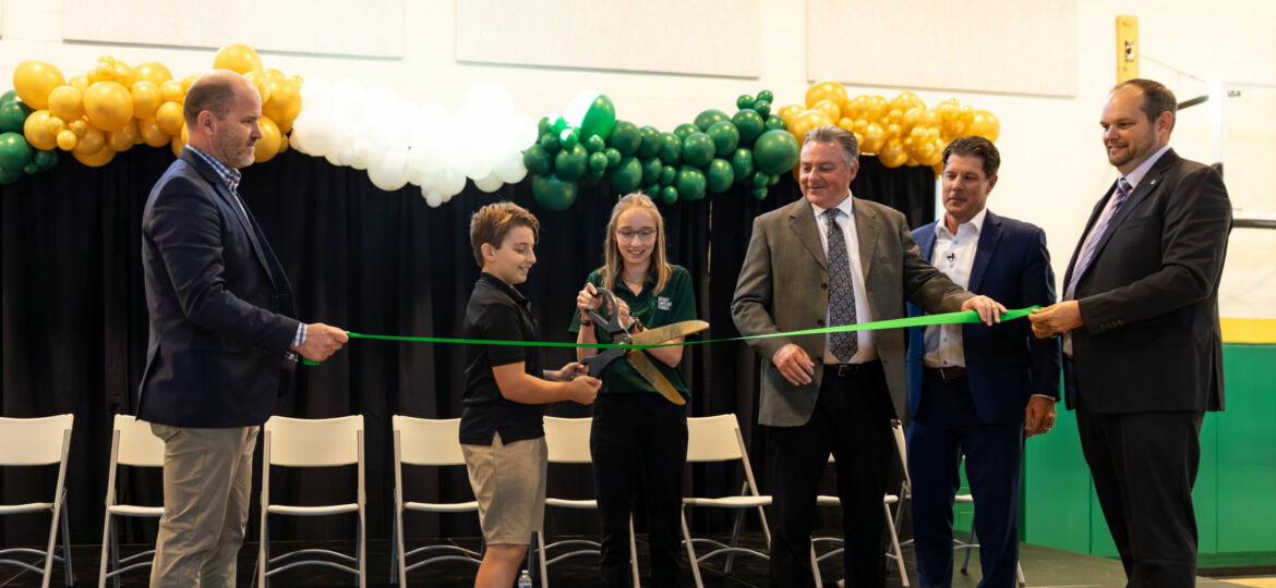 A group of people cutting a green ribbon at the GCS Val Vista Campus, surrounded by balloons.