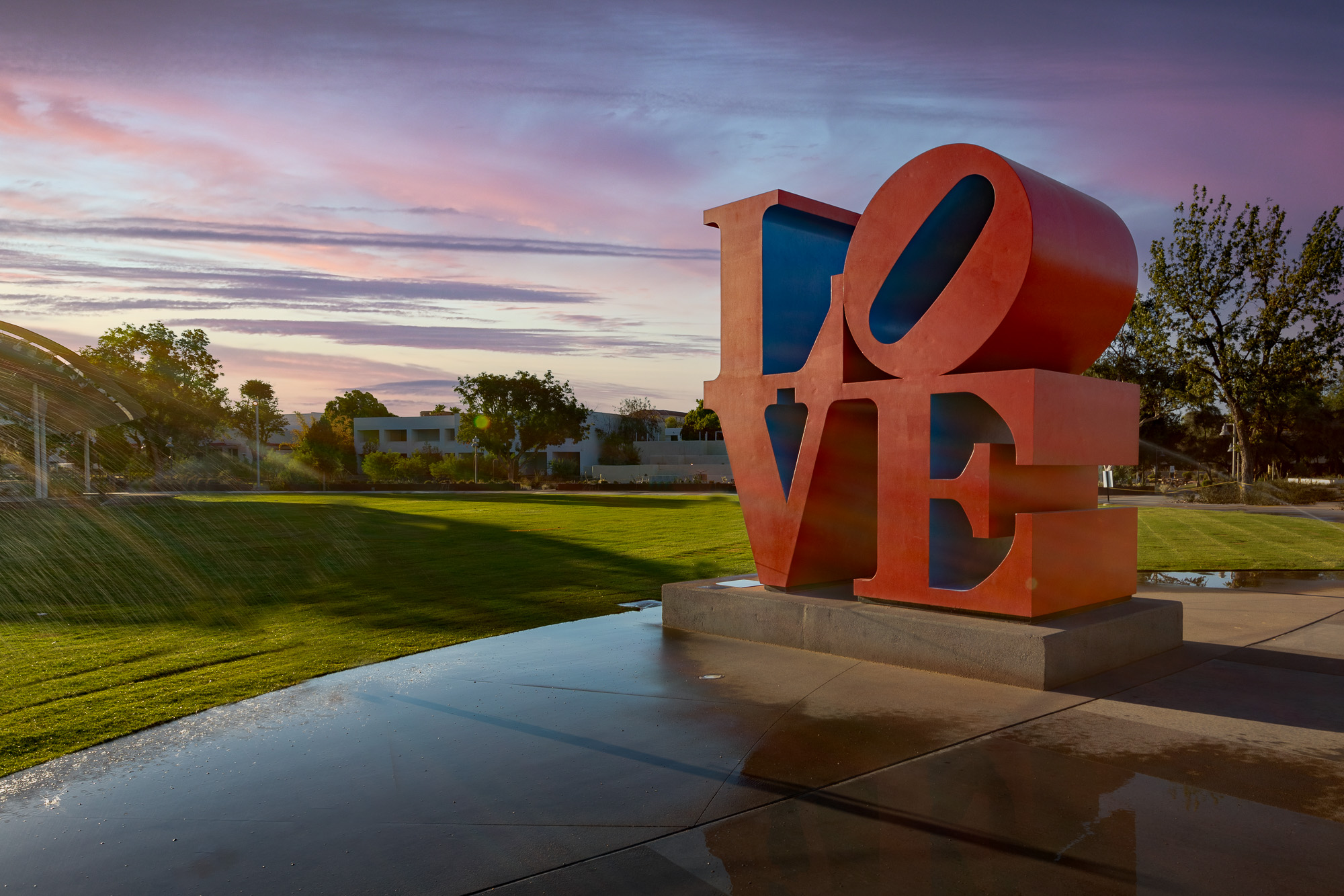 A vibrant red and blue statue of love stands proudly in a park.